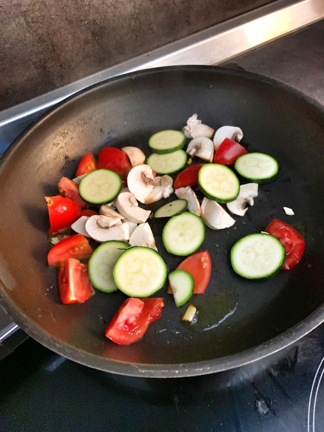 tomatoes, zucchini, and mushrooms in a frying pan.