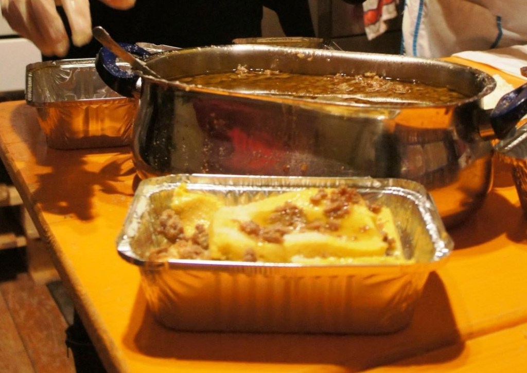 A pan of polenta, sausage, and cheese in front of a pot of sauce