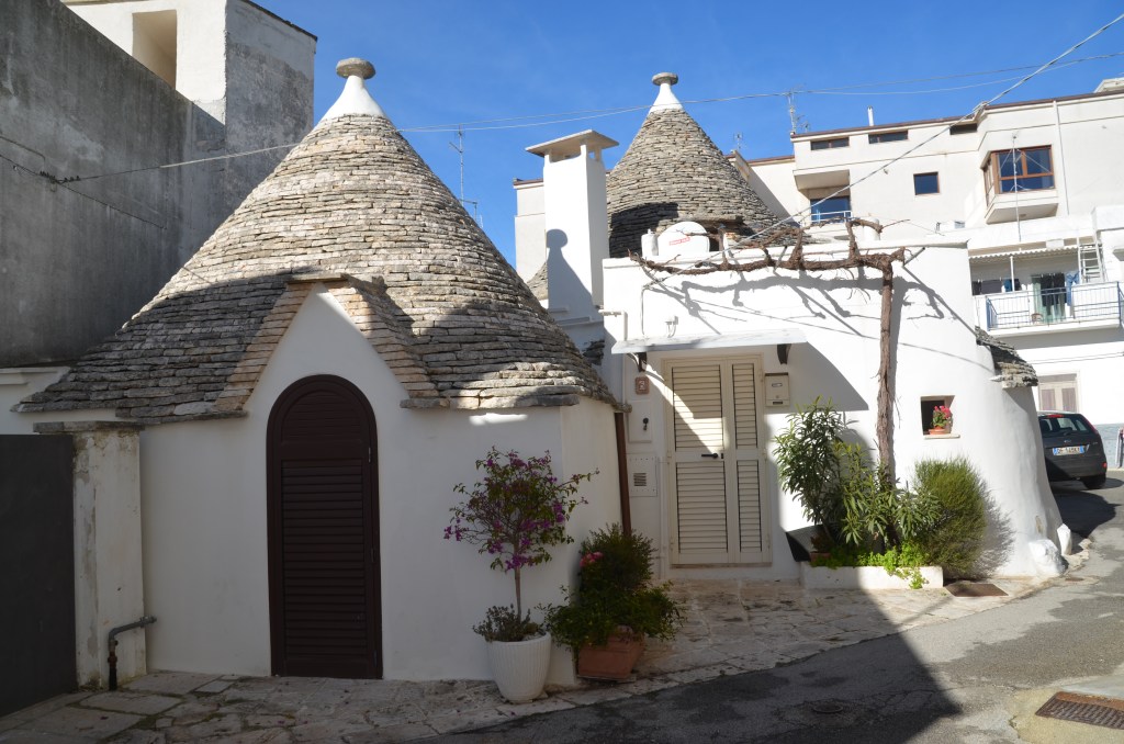 Two trulli with modern apartments in the background