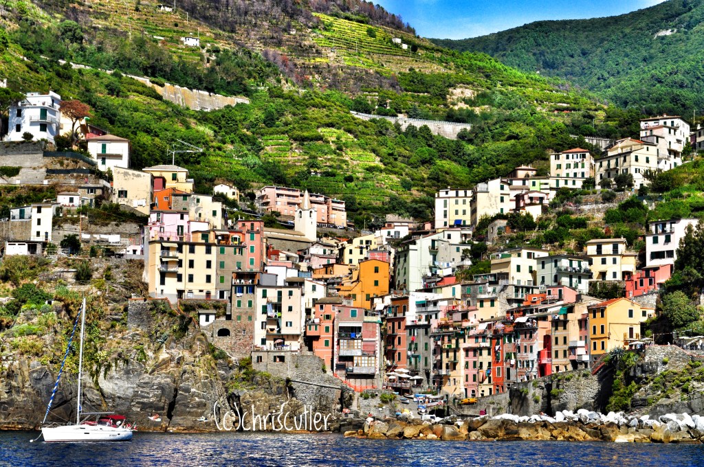Colorful buildings built along the coastal hills; small boat in foreground